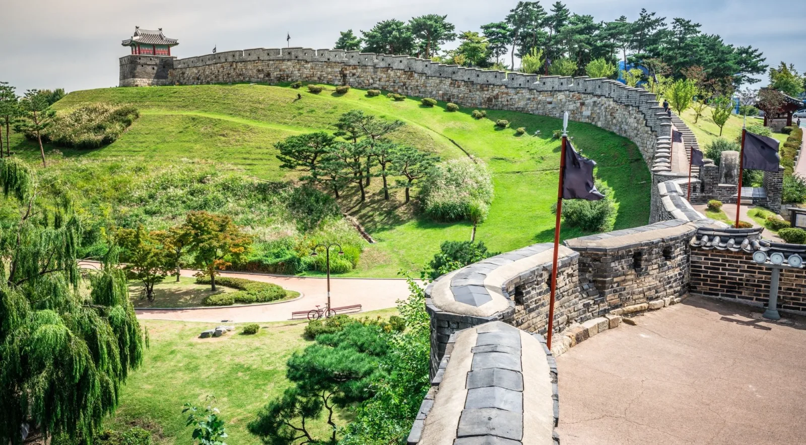 Green rampart curving over a hill with a pavilion and garden path at Hwaseong Fortress