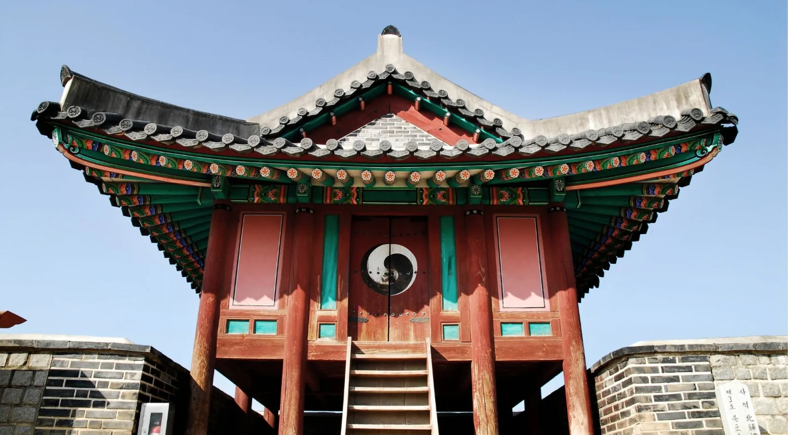 Painted pavilion with a taegeuk roundel and timber steps on the Hwaseong Fortress wall