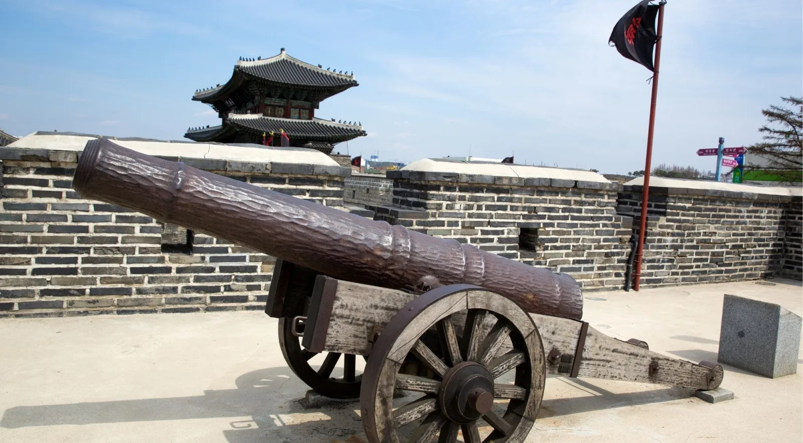 Historic cannon mounted on the Hwaseong Fortress rampart with a pavilion behind