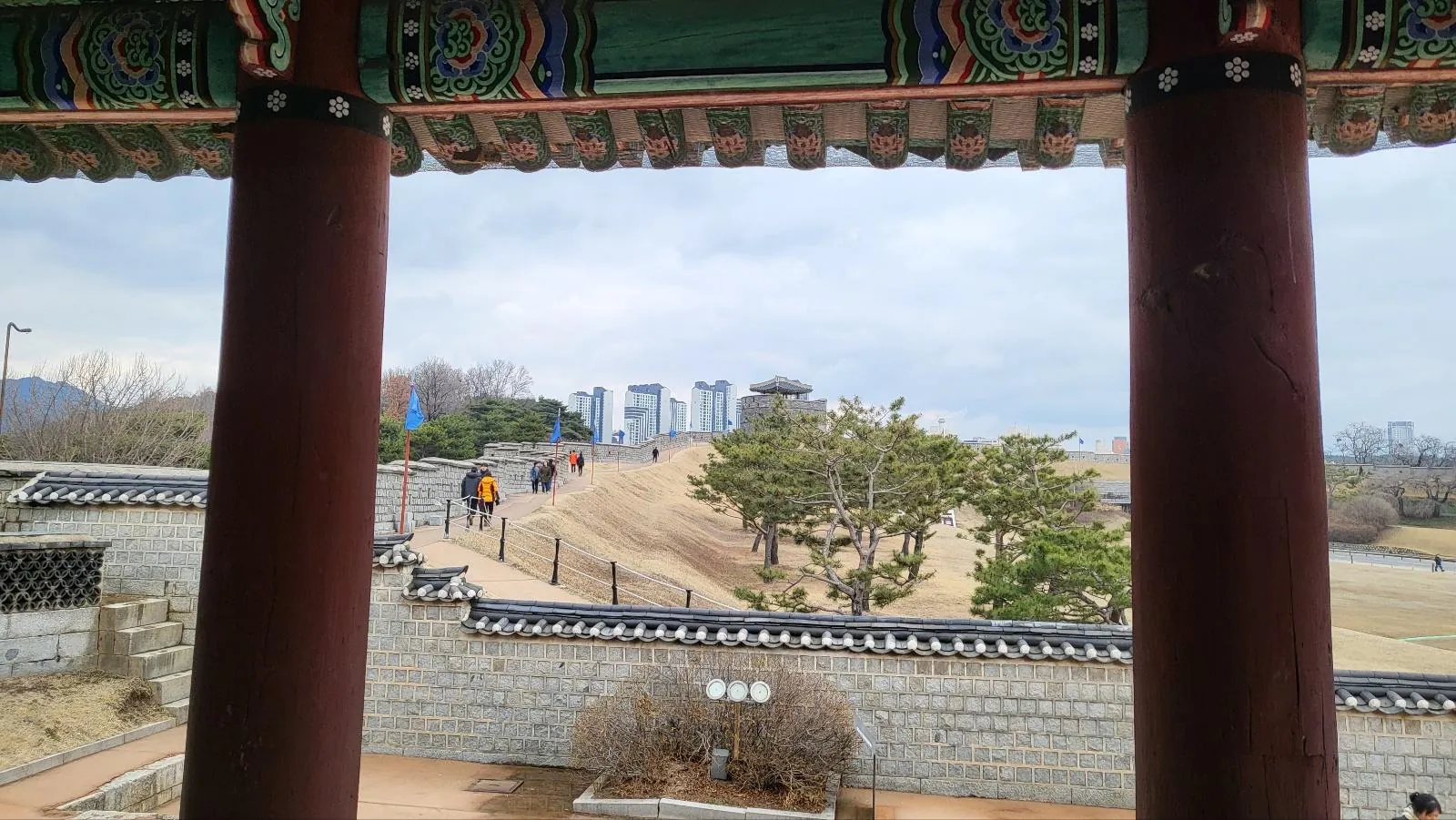 The fortress wall walk seen between the red columns of a Hwaseong pavilion
