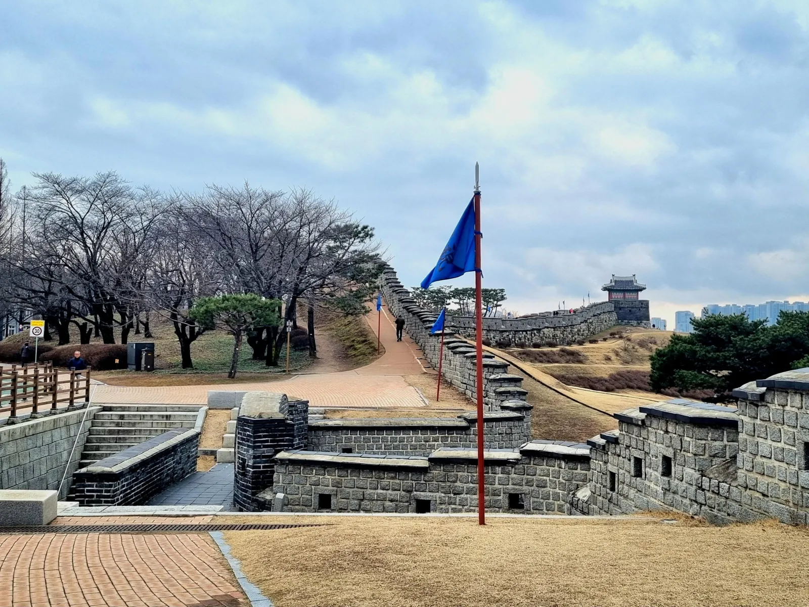 Bare cherry trees and a flag beside the Hwaseong Fortress rampart in early spring