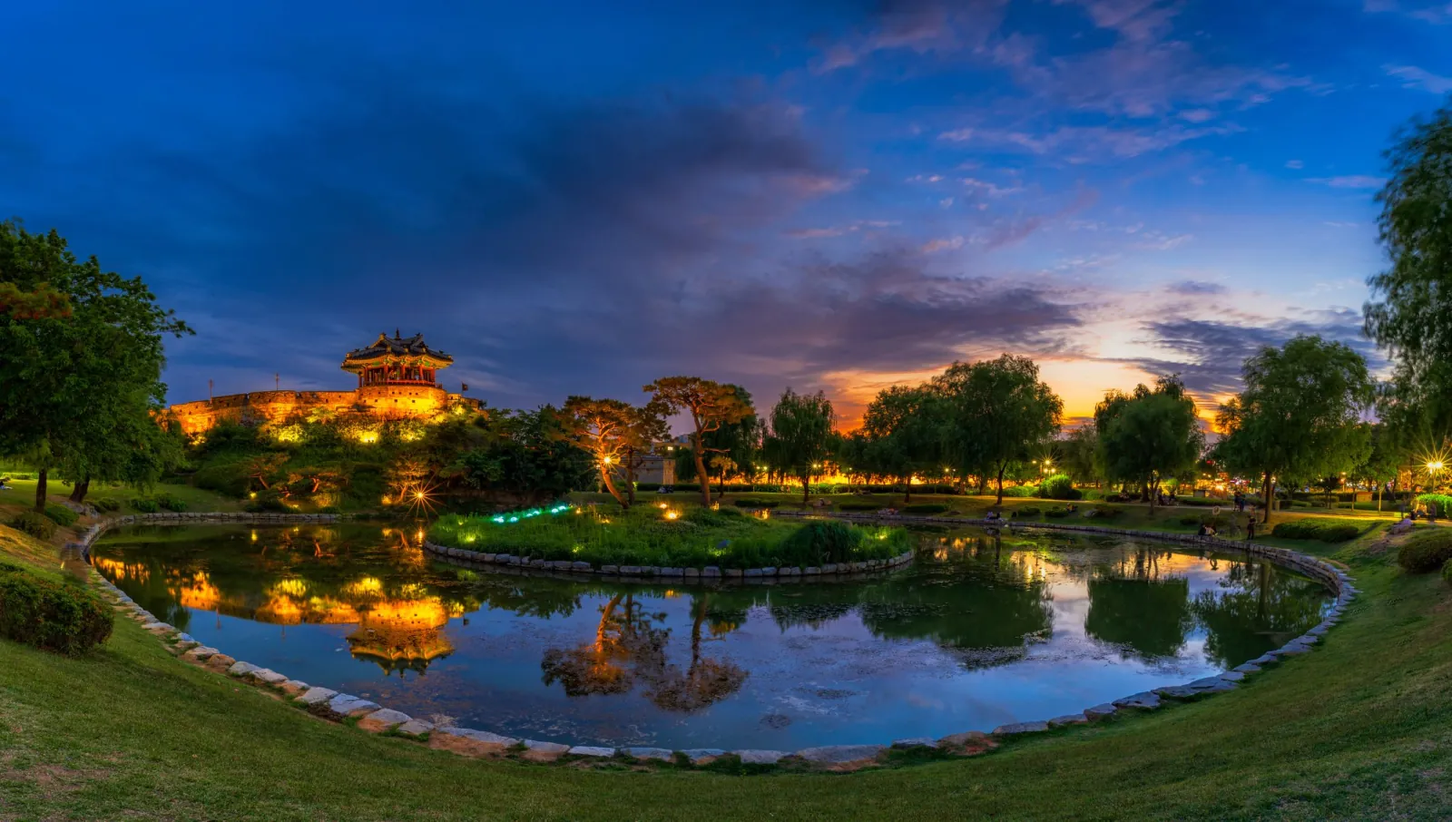 Hwaseong Fortress pavilion and pond lit up at dusk with reflections on the water