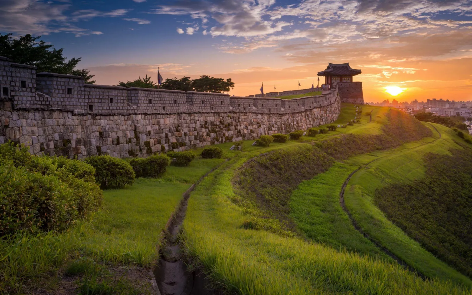 Sunset over the grass rampart and stone wall of Suwon Hwaseong